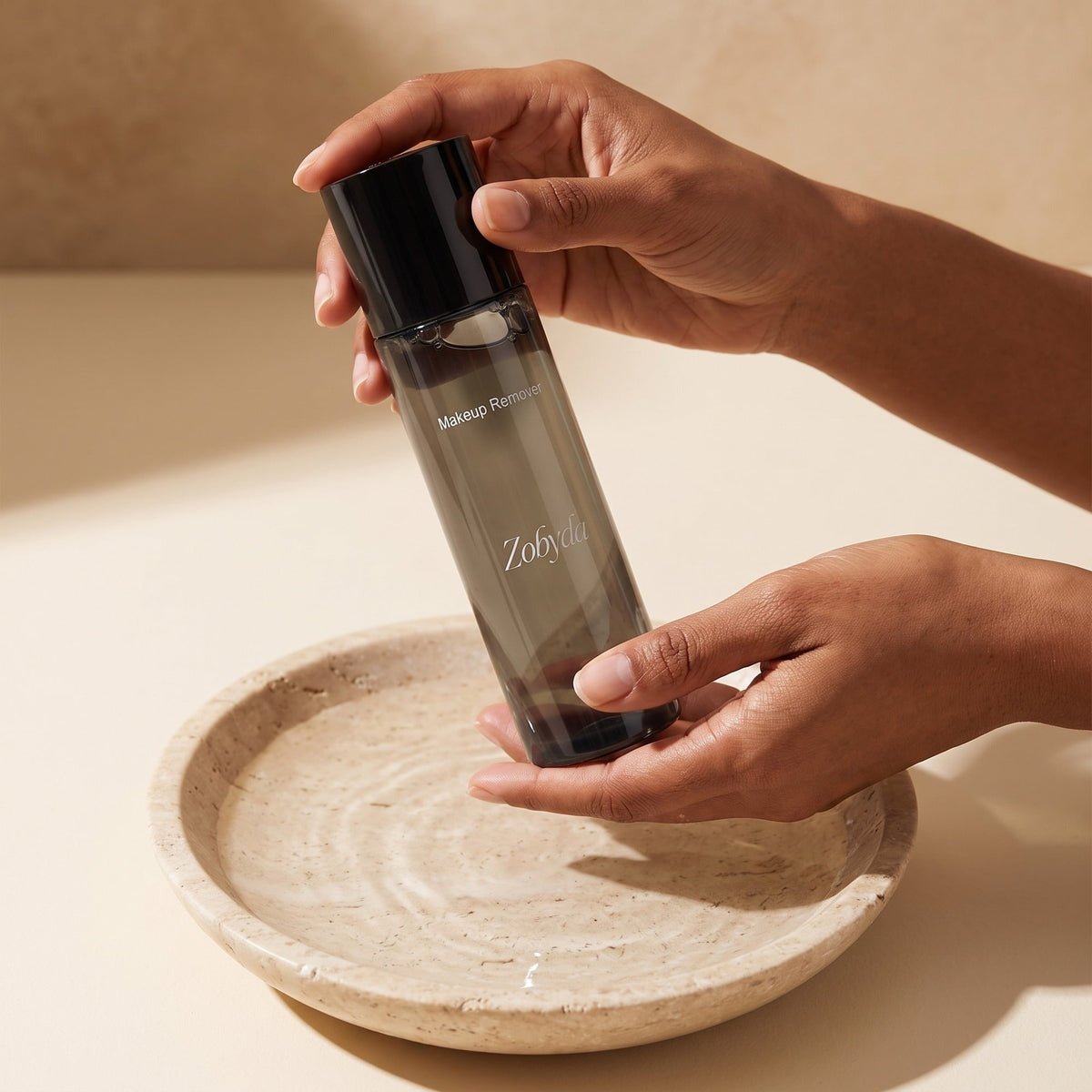 Hands holding the Zobyda Makeup Remover Solution above a dish of water